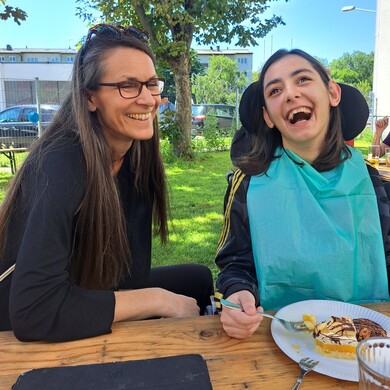 Eine Nutzerin und eine Betreuerin von BALANCE sitzen gemeinsam an einem Tisch im Garten und essen Kuchen.
