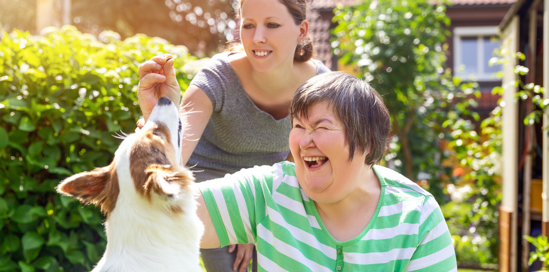 Zwei Frauen spielen mit einem Hund im Garten einer Tagesstruktur f&uuml;r Menschen mit Behinderung.