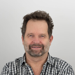 Portr&auml;taufnahme von Mag. Michael Katschnig, Mitarbeiter der Stabstelle Personal bei BALANCE. Er blickt freundlich l&auml;chelnd in die Kamera. Er hat dunkles, leicht gelocktes Haar und einen gepflegten Dreitagebart. Er tr&auml;gt ein schwarz-wei&szlig; kleinkariertes Hemd vor einem neutralen, hellgrauen Hintergrund.