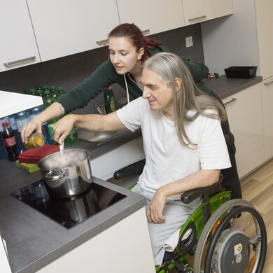 Ein Mann im Rollstuhl und eine Betreuungsperson kochen gemeinsam am Herd.