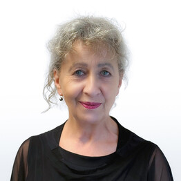 Portr&auml;taufnahme von Cornelia Renoldner, Obfrau des Vereins BALANCE. Sie blickt mit einem freundlichen L&auml;cheln und wachen Augen direkt in die Kamera. Sie hat graues, lockiges Haar, das ihr Gesicht locker umrahmt. Sie tr&auml;gt dunkle, tropfenf&ouml;rmige Ohrringe und ein elegantes schwarzes Oberteil mit leicht transparenten &Auml;rmeln vor einem neutralen, hellen Hintergrund.