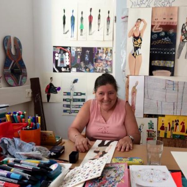 Eine Nutzerin von BALANCE sitzt im Kunst-Atelier an einem Tisch mit vielen gemalten Bildern.