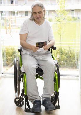 Ein Mann sitzt im Rollstuhl und h&auml;lt ein Buch in der Hand.