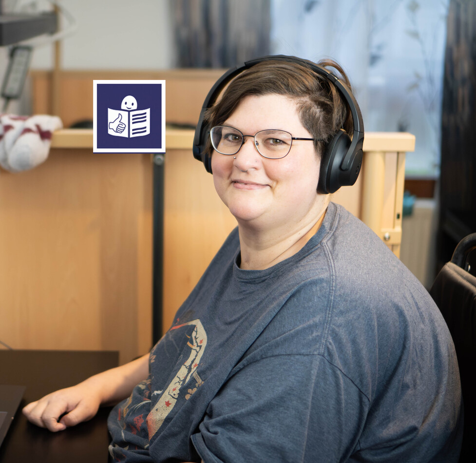 Eine Frau mit Brille und Kopfhörern sitzt lächelnd an einem Schreibtisch. Vor ihr steht ein aufgeklappter Laptop. Über ihr ist das blau-weiße Logo für „Leicht Lesen“ eingeblendet.