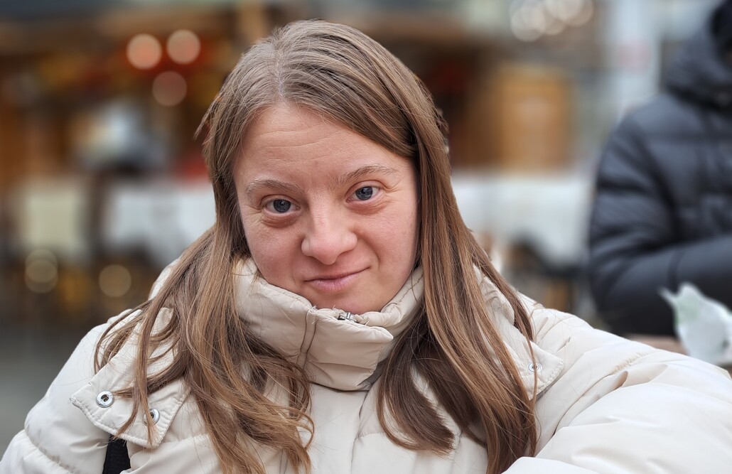Eine junge Frau mit Behinderung und langen braunen Haaren blickt selbstbewusst in die Kamera.