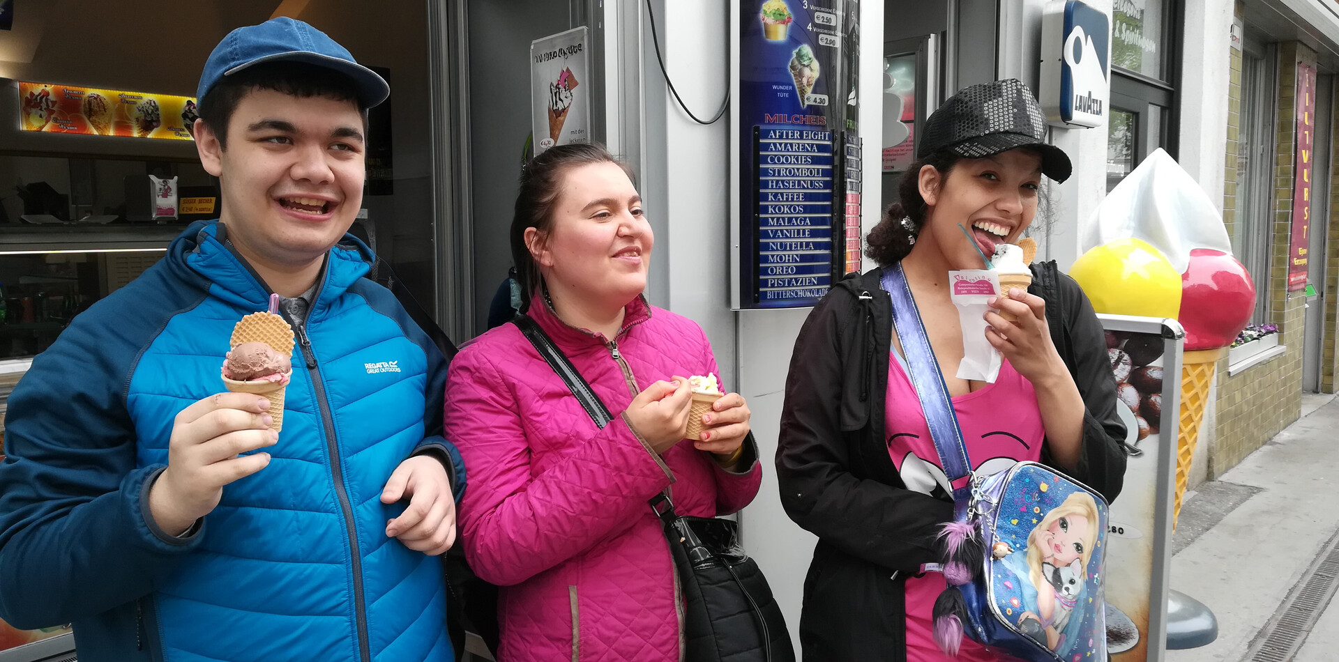 Ein jungern Mann und zwei Frauen stehen vor einem Eisgesch&auml;ft. Sie haben alle jeweils ein Eis in der Hand und lachen.