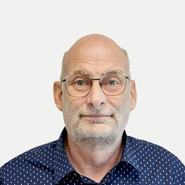 Wolfgang Paschinger Porträtaufnahme von Wolfgang Paschinger, Leiter für Fuhrpark und Gebäude bei BALANCE. Er blickt mit einem freundlichen Lächeln direkt in die Kamera. Er hat eine Glatze, einen grauen Dreitagebart und trägt eine markante Brille mit dünnem Metallrahmen. Er trägt ein dunkelblaues Hemd mit einem feinen weißen Punktmuster vor einem neutralen, hellgrauen Hintergrund.