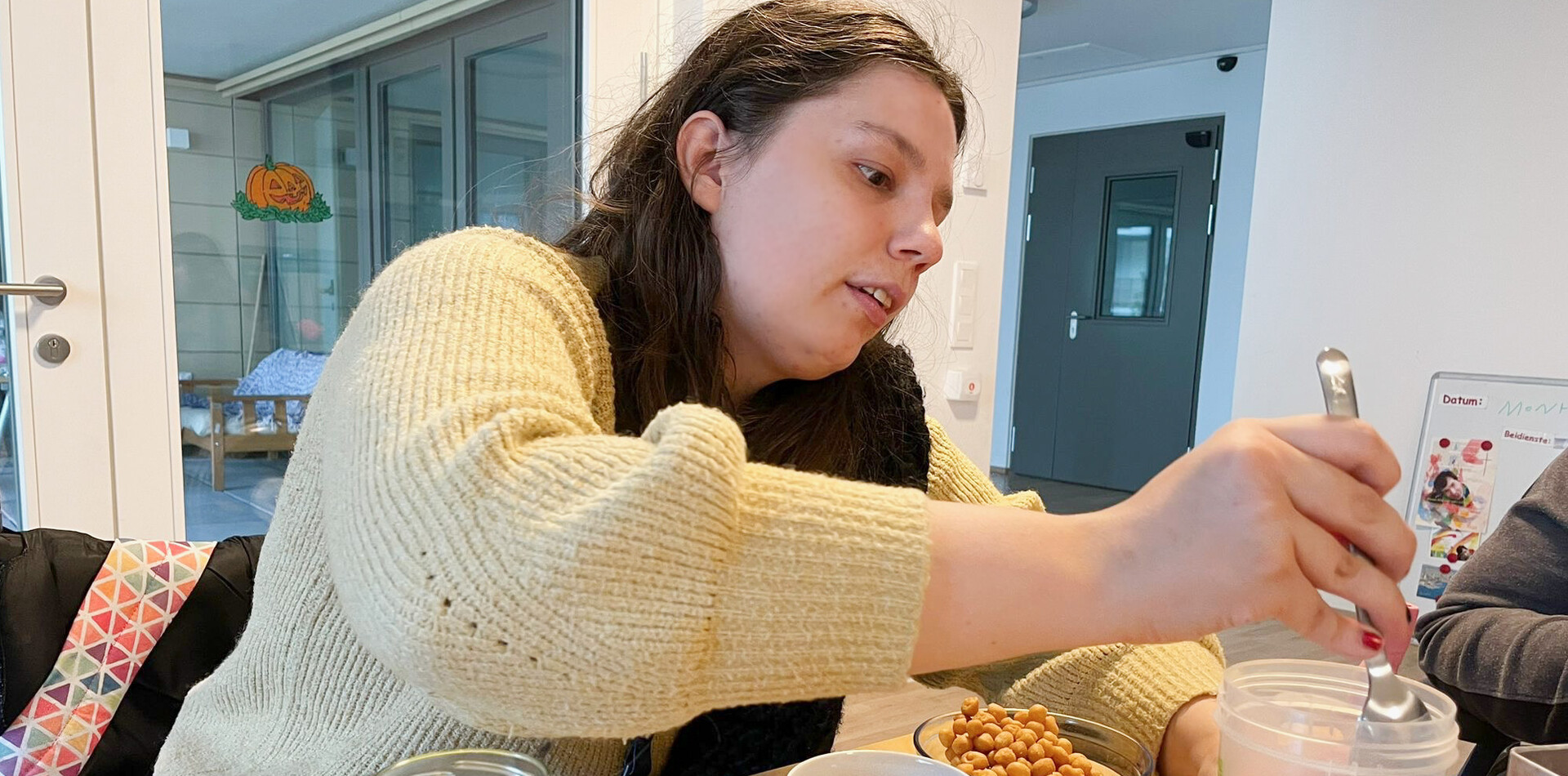 Frau bereitet an einem Tisch Essen vor und f&uuml;llt Kichererbsen in einen Beh&auml;lter &ndash; eine Alltagssituation beim selbstst&auml;ndigen Wohnen.