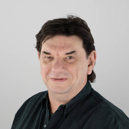 Martin Nemeth Porträtaufnahme von Martin Nemeth, Leitung der Tagesstruktur Fuchsenfeld bei BALANCE. Er blickt mit einem freundlichen, dezenten Lächeln direkt in die Kamera. Er hat dunkles, kurzes Haar und trägt ein dunkelgrünes Hemd vor einem neutralen, hellgrauen Hintergrund.