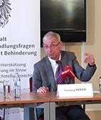 Dr. Hansjörg Hofer hinter einem Tisch sitzend, vor ihm ein weisses Schild mit seinem Namen.